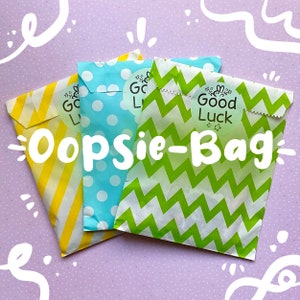 May include: Three small paper bags with different patterns. The bags are labeled "Good Luck" and "Oops-Bag".