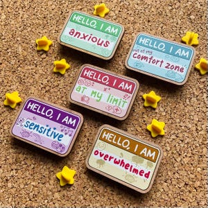 May include: Five wooden pins with colorful backgrounds and black text. Each pin says "Hello, I am" followed by a different word: anxious, out of my comfort zone, at my limit, sensitive, overwhelmed.