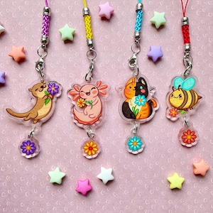 Könnte beinhalten: Vier bunte Acryl-Anhänger mit einem Cartoon-Otter, Axolotl, Katze und Biene, die jeweils eine Blume halten. Die Anhänger sind an bunten Schnüren befestigt und haben einen kleinen Blumenanhänger, der darunter baumelt.