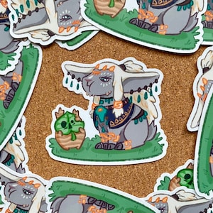 May include: A sticker featuring a gray rabbit-like creature with ornate details, including a decorative collar and headpiece. The sticker also includes a small, green plant character. The design has a fantasy theme.