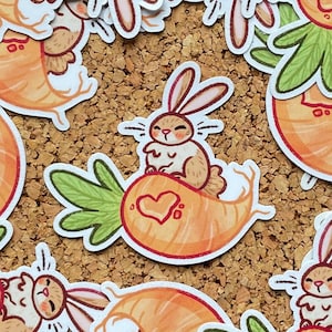 Könnte beinhalten: Eine Sammlung von Aufklebern mit einem Cartoon-Hasen, der auf einer Karotte reitet. Der Hase ist hellbraun mit langen Ohren, und die Karotte ist orange mit grünen Blättern. Auf der Karotte ist ein Herz gezeichnet.