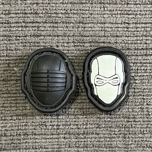 以下が含まれることがあります： マスクのデザインが施された黒と白のパッチが2つ。左のパッチは、テクスチャ加工されたデザインの黒いマスク。右のパッチは、黒いデザインの白いマスクです。