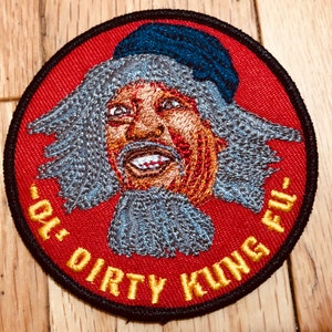 Op de afbeelding: Gestikt patch met een rode achtergrond en een gele rand. De patch toont een cartoon afbeelding van een man met grijs haar en een blauwe hoed. De tekst "Ol' Dirty Kung Fu" is in geel rond de afbeelding geschreven.