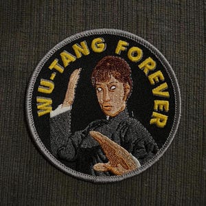 以下が含まれることがあります： 黄色で「WU-TANG FOREVER」の文字が入った丸い刺繍パッチ。武道のポーズをとる人物の様式化された画像が特徴です。背景は黒で、灰色の縁取りがあります。パッチは濃い緑色の生地にあります。