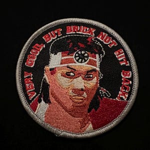 May include: Circular embroidered patch with a martial artist design. The patch features a portrait of a person with a headband and the text "VERY GOOD, BUT BRICK NOT HIT BACK". The color scheme includes red, black, and tan, with a white border.