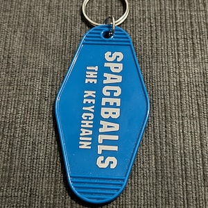 May include: Blue keychain shaped like a motel key with the text "Spaceballs The Keychain" in white lettering.