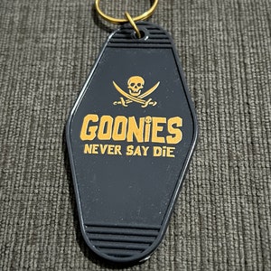 May include: Black Goonies keychain with a gold skull and crossbones and the text "Goonies Never Say Die".