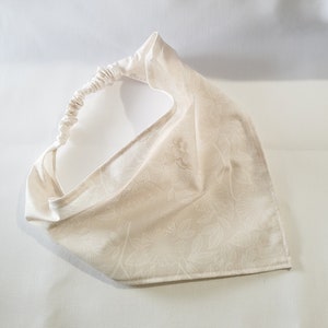 May include: A white cotton headband with a floral pattern. The headband has a gathered elastic band for a comfortable fit.