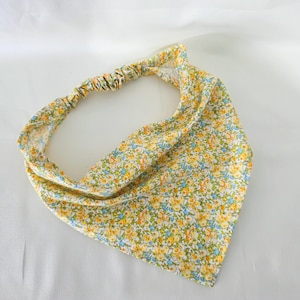 May include: A floral headband with a pattern of yellow, blue, and orange flowers. The elasticated back ensures a comfortable fit. The headband is designed to be worn around the head.