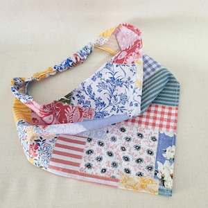 May include: A patchwork headband featuring a variety of floral, striped, and patterned fabrics in shades of red, blue, yellow, and white. The headband has an elastic band for a comfortable fit and a decorative fabric panel.
