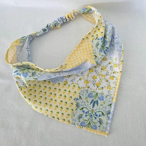 Può includere: Una bandana triangolare per capelli con un design patchwork di motivi floreali gialli e blu, piccoli limoni gialli e un motivo a quadretti vichy giallo e bianco. L'accessorio include una fascia elastica sul retro per una tenuta sicura.
