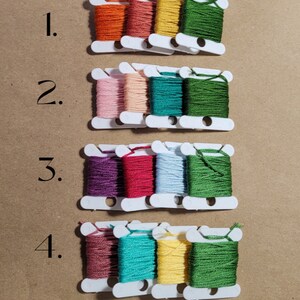 May include: Four rows of embroidery floss spools, each row with four spools. Row 1: orange, red, yellow, green. Row 2: pink, beige, teal, green. Row 3: purple, red, light blue, green. Row 4: brown, teal, yellow, green. The rows are numbered 1 through 4.