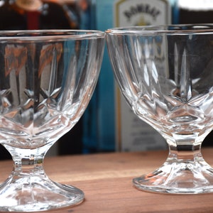 May include: Two clear glass dessert bowls with a diamond pattern on the sides and a pedestal base. The bowls are empty and sitting on a wooden surface.