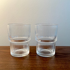 May include: Two clear glass drinking glasses with a ribbed design. The glasses are stacked on top of each other.