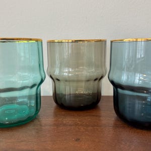 May include: Three glass tumblers with gold rims. The tumblers are teal, gray, and blue.