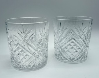 May include: Two clear glass tumblers with a diamond-shaped cut pattern. The glasses are empty and sitting on a white surface.