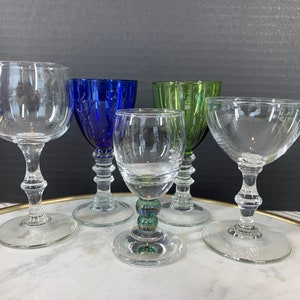 May include: Four stemmed drinking glasses, one clear, one blue, one green, and one with a clear stem and a green and blue iridescent base.