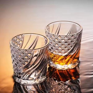 May include: Two clear glass tumblers with a swirling, textured design. The larger tumbler is filled with a golden amber liquid.