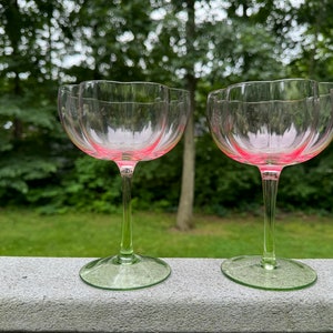 May include: Two clear glass stemmed drinking glasses with a pink rim and a green stem. The glasses have a scalloped edge.