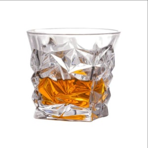 May include: A clear glass whiskey tumbler with a geometric, faceted design. The glass is filled with amber-colored whiskey.