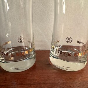 Puede incluir: Dos vasos de beber de vidrio transparente con letras doradas que dicen "Brewery & Distillery" y un c&iacute;rculo dorado con el n&uacute;mero "60" en su interior.