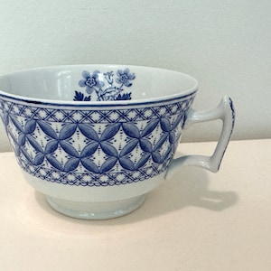 May include: A white teacup with a blue and white floral pattern. The cup has a wide, rounded shape and a single handle.