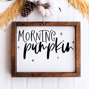 May include: A wooden framed sign with a white background and black lettering that reads "Morning Pumpkin". The sign is decorated with small white stars.
