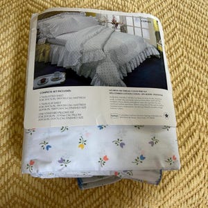 May include: A complete twin-size Copley bed sheet set. The set includes a fitted sheet, flat sheet, and a standard pillowcase. The sheets are white with a floral pattern and a ruffled edge. The packaging includes the dimensions of the sheets in inches and centimeters.