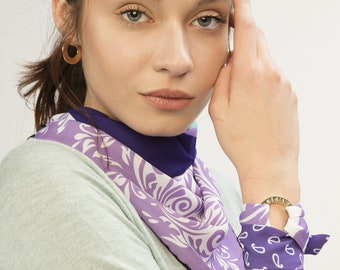 May include: A woman wearing a purple and white patterned scarf with a gold bracelet. The scarf has a blue trim.