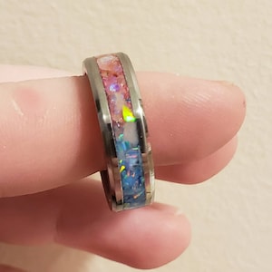 Puede incluir: Un anillo de plata con una banda de purpurina iridiscente rosa, blanca y azul.