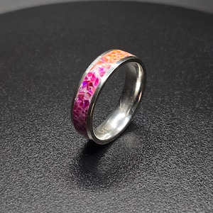 Può includere: Un anello d'argento con una fascia a motivi rosa, arancio e bianco.