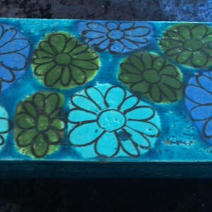 Puede incluir: Una caja de cerámica azul con un diseño floral. La caja está decorada con flores azules, verdes y blancas.