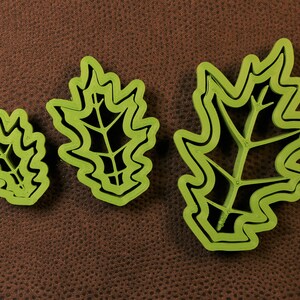 May include: Three green plastic cookie cutters shaped like oak leaves. The cutters are different sizes, with the largest cutter being about 6 inches long.