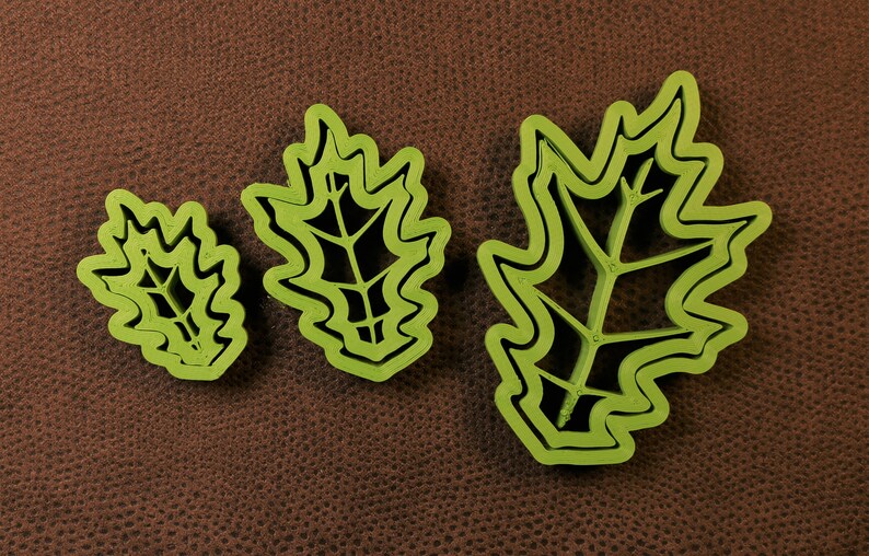 May include: Three green plastic cookie cutters shaped like oak leaves. The cutters are different sizes, with the largest cutter being about 6 inches long.