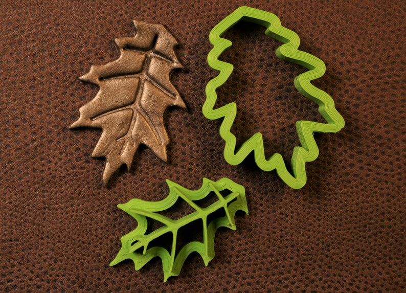 May include: Three leaf-shaped cookie cutters, two green and one brown. The green cutters are detailed with a raised vein pattern. The brown cutter is a solid leaf shape.