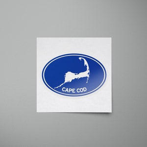 May include: A blue oval sticker with a white outline. The sticker features a white silhouette of Cape Cod, Massachusetts, with the text "CAPE COD" printed below the silhouette.