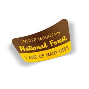 May include: A brown and yellow sticker with the text "White Mountain National Forest" and "Land of Many Uses".