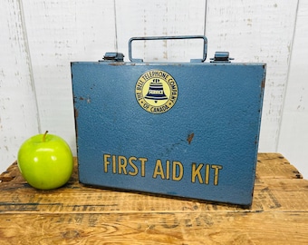 May include: Blue metal first aid kit with a yellow and black logo that reads "The Bell Telephone Company of Canada" and a bell icon. The text "First Aid Kit" is printed in yellow on the front.