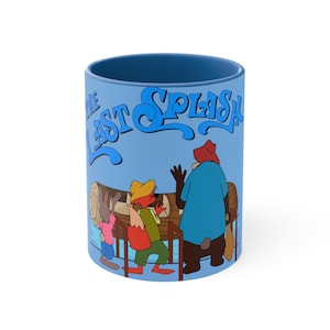 Può includere: Una tazza in ceramica blu con un'illustrazione di tre animali dei cartoni animati. Il testo "The Last Splash" è stampato in blu sulla tazza.