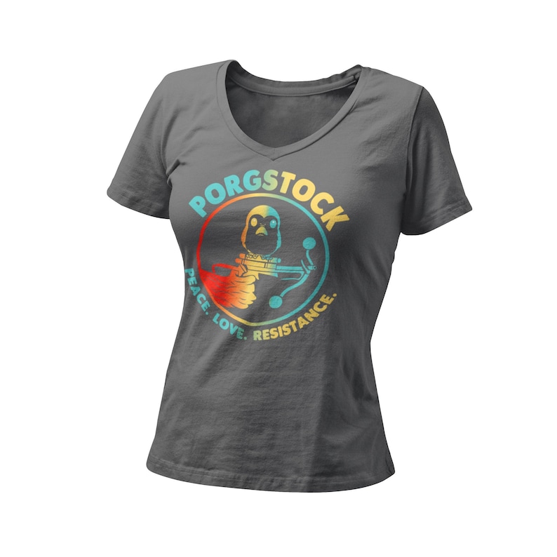 Puede incluir: Una camiseta gris oscuro de cuello en V con un gr&aacute;fico colorido de un porg sosteniendo un bl&aacute;ster. El gr&aacute;fico est&aacute; en un c&iacute;rculo con el texto "Porgstock" sobre el porg y "Peace. Love. Resistance." debajo del porg.