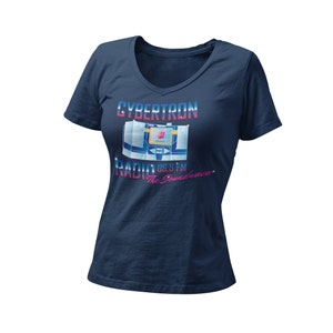 Puede incluir: Una camiseta azul marino con un gráfico de una radio de estilo retro con el texto "Cybertron Radio 86.8 FM The Soundwave" impreso en la parte delantera.