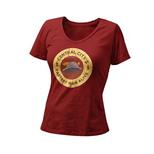May include: A maroon V-neck t-shirt with a circular graphic. The graphic features a winged hat and the text "CENTRAL CITY'S FASTEST MAN ALIVE" in a distressed, vintage style. The shirt is made of a soft material.