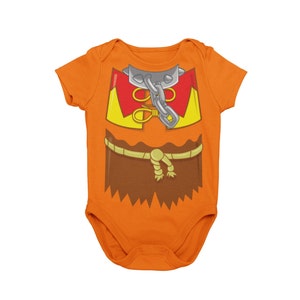May include: Orange baby onesie with a cartoon image of a brown-skinned person wearing a red and yellow shirt with a chain around their neck and a brown rope belt.