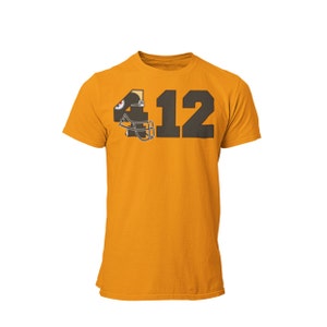 Peut inclure: Un t-shirt jaune avec un design de casque de football noir et or et le numéro "412" imprimé sur le devant.