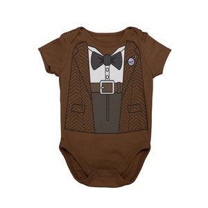 Puede incluir: Un body de bebé marrón con una imagen impresa de un traje marrón, una camisa blanca, una pajarita negra y un cinturón. El traje tiene un patrón de espiga. El body tiene mangas cortas.
