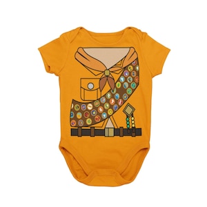 May include: A yellow baby onesie with a brown scout uniform design. The design includes a brown sash with colorful badges, a brown belt, and a brown neckerchief with a yellow knot.