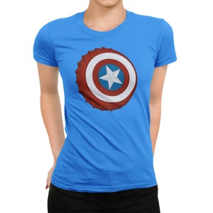 May include: A light blue t-shirt featuring a graphic of a shield with a white star on a blue circle, surrounded by a red and white design. The shirt is a crew neck and short-sleeved.