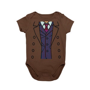 May include: A brown baby onesie with a cartoon image of a suit and tie on the front. The suit is blue with red stripes and a pink tie.
