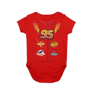 May include: Red baby onesie with a graphic of Lightning McQueen from Cars. The onesie features McQueen's racing number "95" and sponsors like Dinoco and Rust-eze.