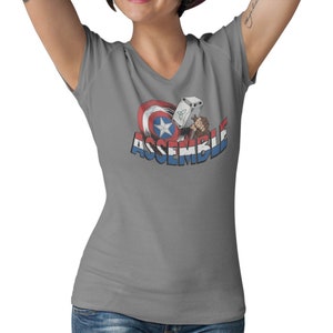 Puede incluir: Camiseta gris de cuello en V con un gr&aacute;fico del escudo del Capit&aacute;n Am&eacute;rica y el martillo de Thor con el texto "ASSEMBLE".